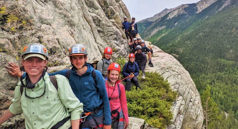 a group of people wearing safety gear stand on a rocky overlook at high elevation